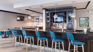 A bar area with a dark wood bar counter, blue bar stools, and hanging pendant lights.