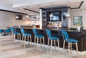 A bar area with a dark wood bar counter, blue bar stools, and hanging pendant lights.