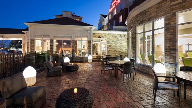 A hotel patio with outdoor seating, a stone floor, and a view of the Hilton Garden Inn building.