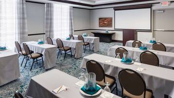 A conference room with multiple tables, chairs, a projector screen, and a carpeted floor.