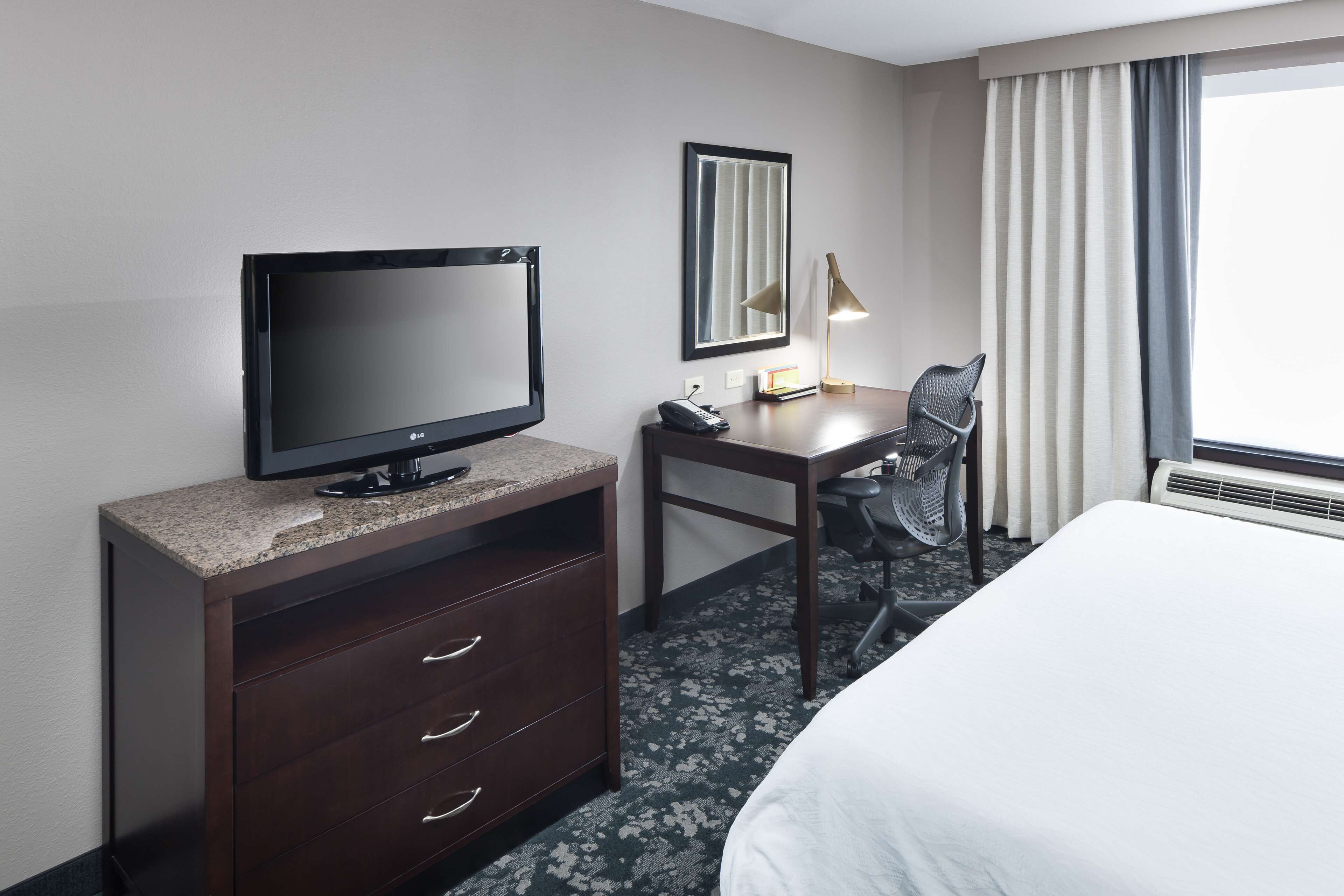 A hotel room with a bed, a desk with a computer, a television, and a chair.