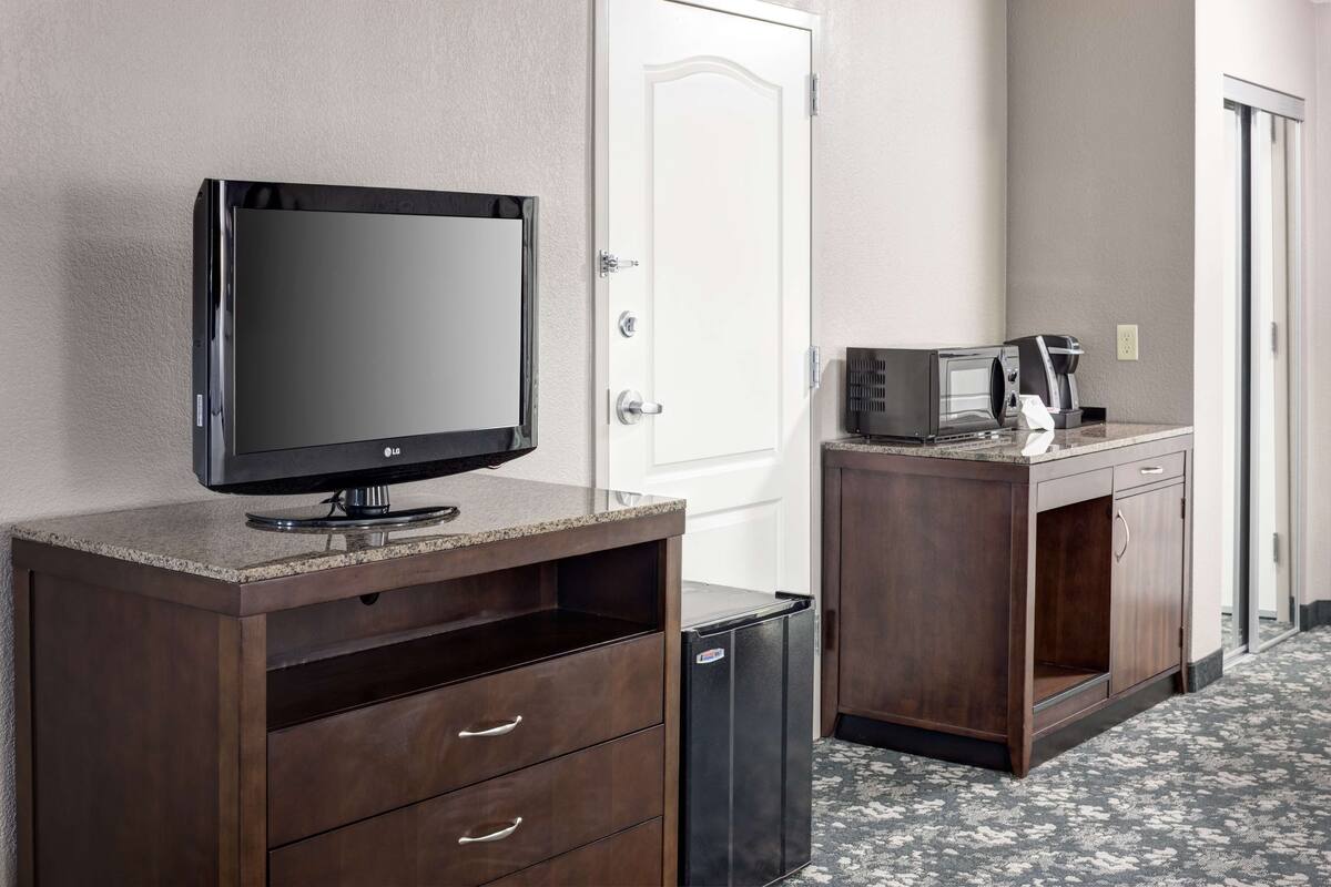 A hotel room with a flat-screen TV on a wooden cabinet, a microwave, and a small trash bin.