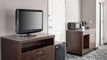 A hotel room with a flat-screen TV on a wooden cabinet, a microwave, and a small trash bin.