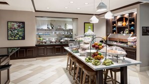 A modern kitchen with a marble countertop, wooden stools, and a fruit display.