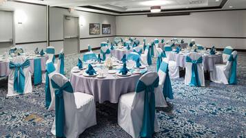 Un salón de conferencias con mesas redondas, sillas blancas con cintas turquesa y alfombra azul.