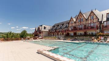Experience the charm of traditional European architecture at this hotel, surrounded by lush trees and a serene pool area with lounge chairs and umbrellas.