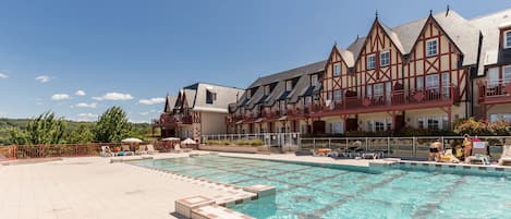 Un hotel con piscina, mobiliario exterior y vistas a las montañas.