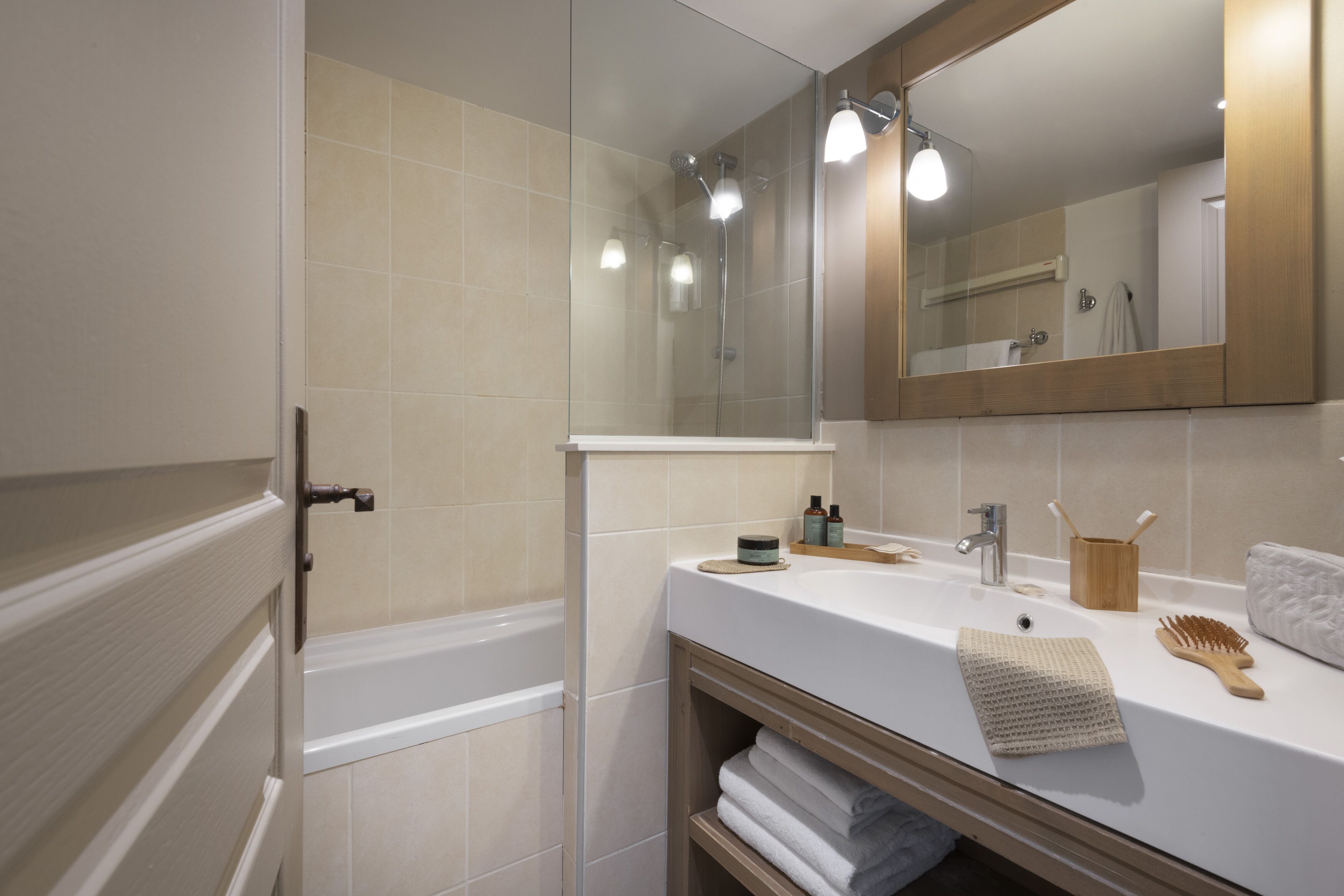 A modern bathroom with a bathtub, a sink with toiletries, and a large mirror.
