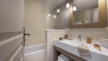 A modern bathroom with a bathtub, a sink with toiletries, and a large mirror.