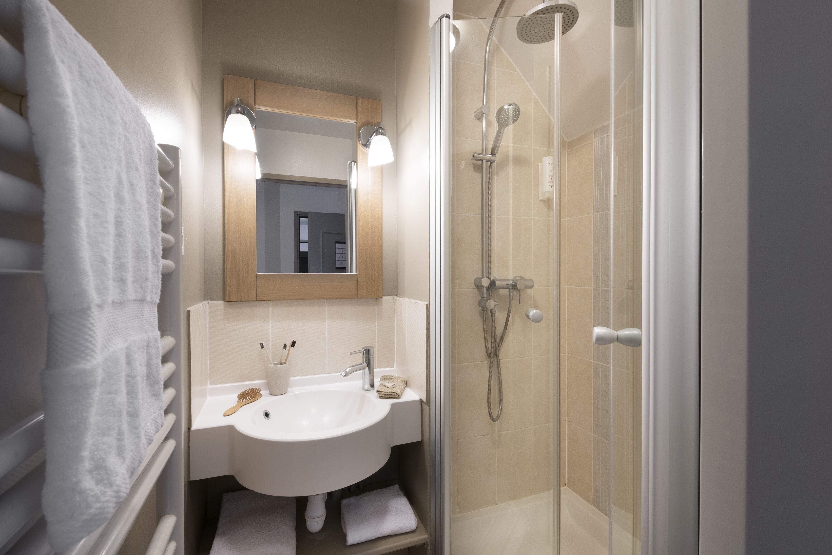 Un baño con lavamanos, espejo, toallero y ducha.
