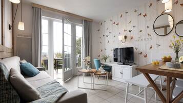 A modern living room with a sofa, a coffee table, and a TV. There is a dining area with a table and chairs.