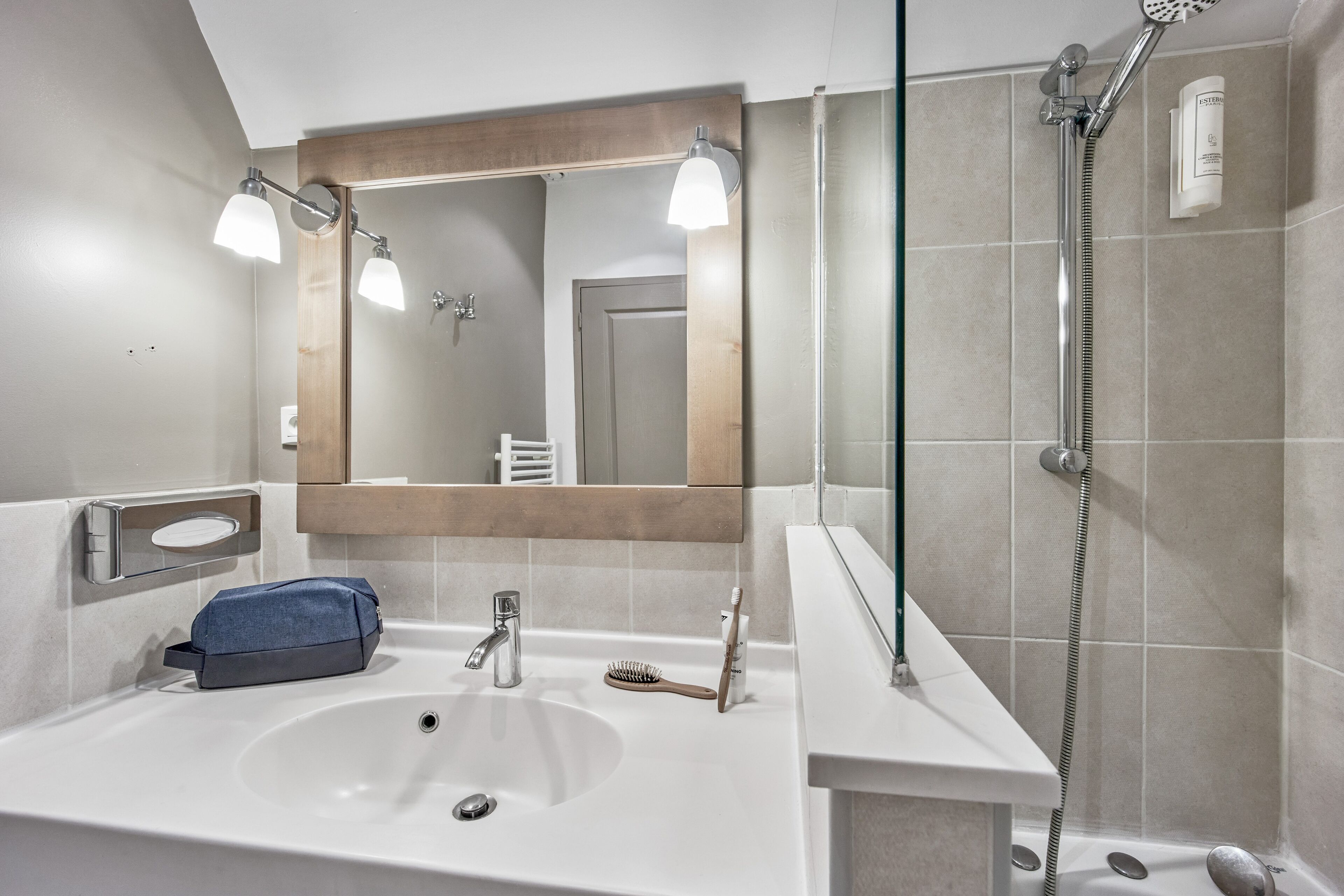 A modern bathroom with a large mirror, a sink, a shower, and a towel rack.