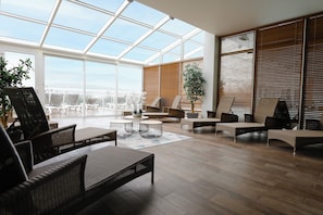 A spacious indoor area with a high ceiling and large windows, featuring wicker furniture and a wooden floor. - Résidence Premium & Spa Houlgate - Pierre & Vacances (Houlgate)
