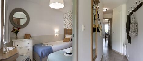 A bedroom with a bed, bedside table, dresser, mirror, and a hallway leading to a dining area.