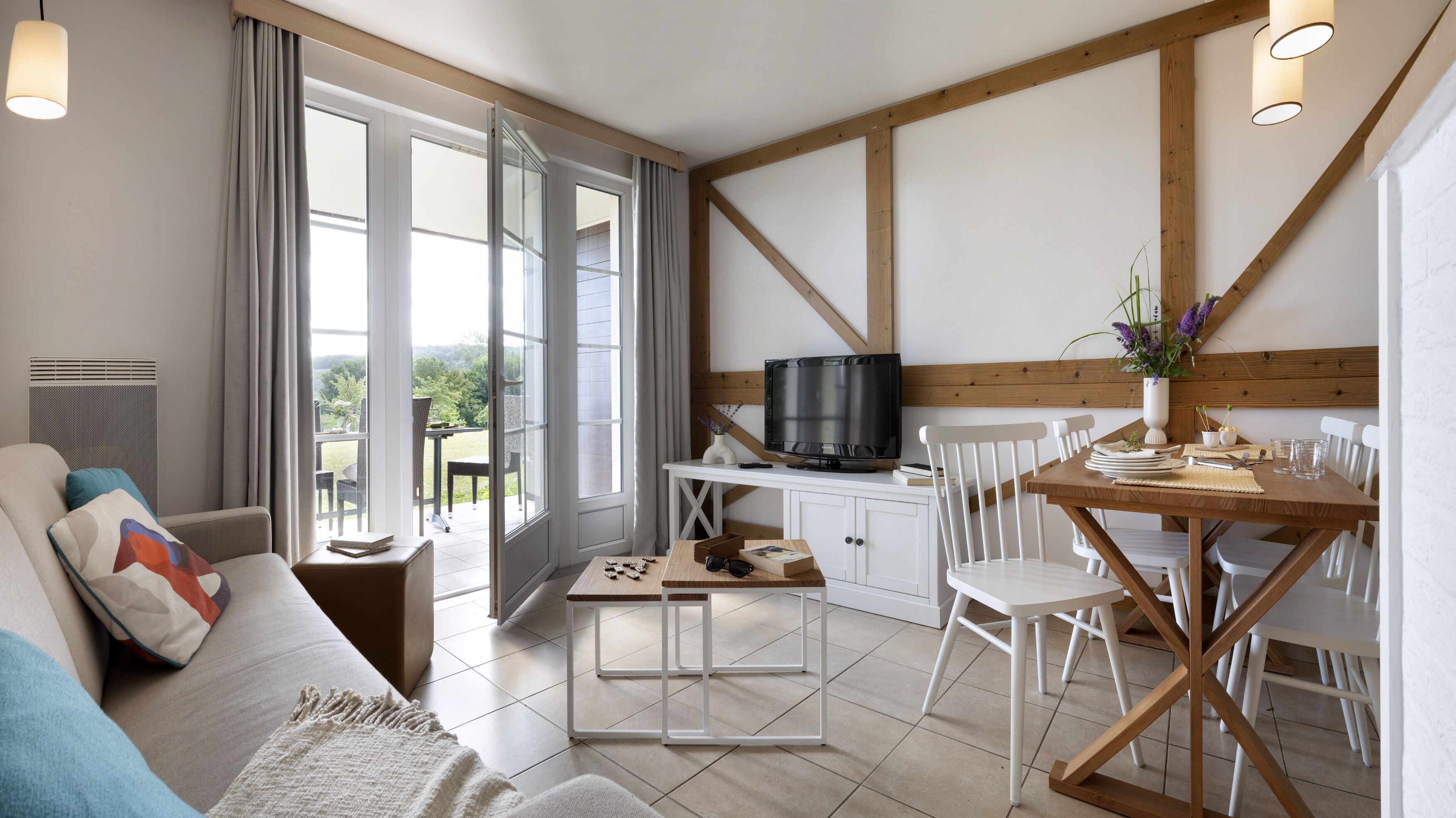 Una sala de estar moderna con un sofá, una mesa de comedor con sillas, un televisor y vistas al exterior.