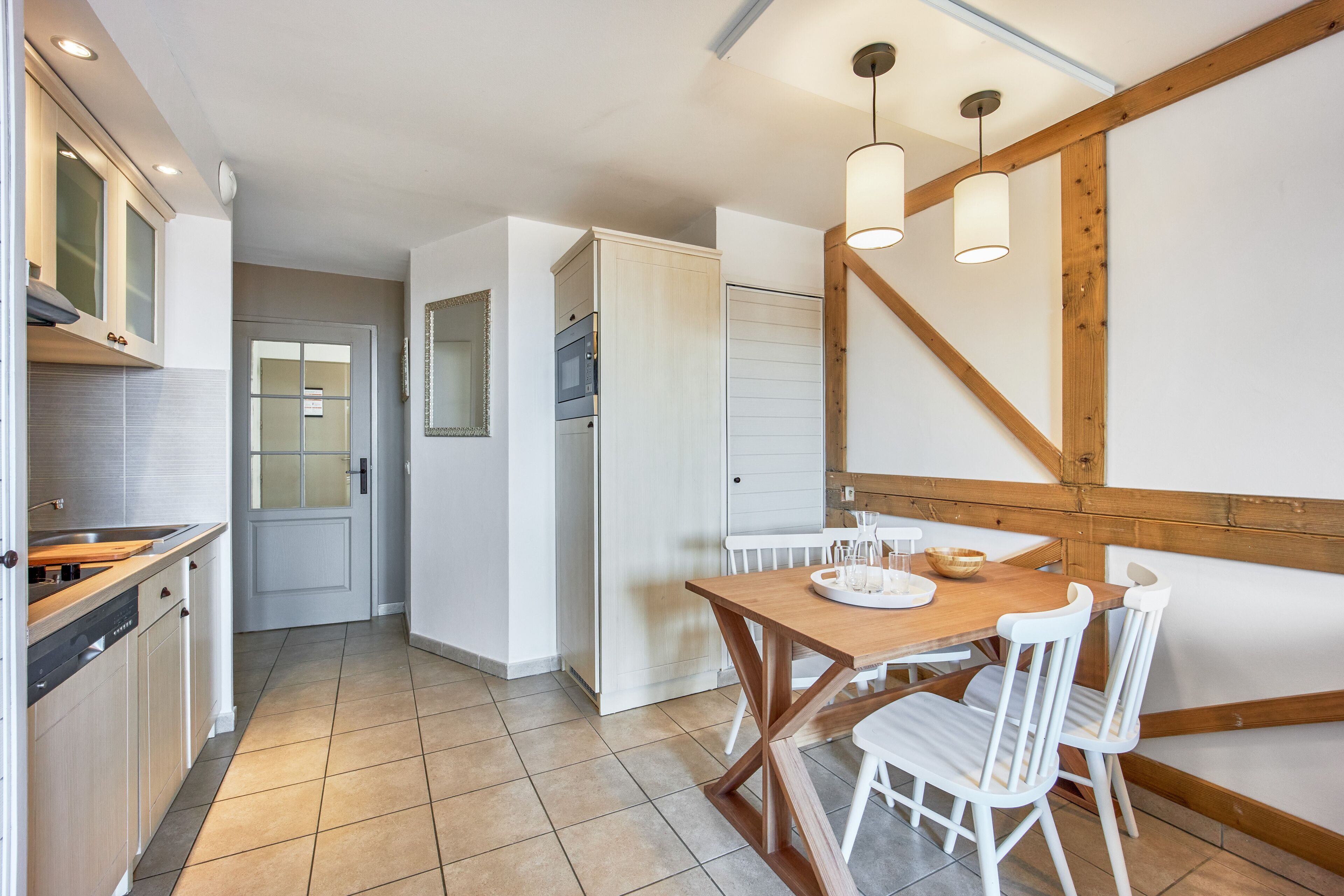 Una cocina moderna con una mesa de comedor de madera y sillas blancas, un horno empotrado y un espejo grande sobre el lavamanos.