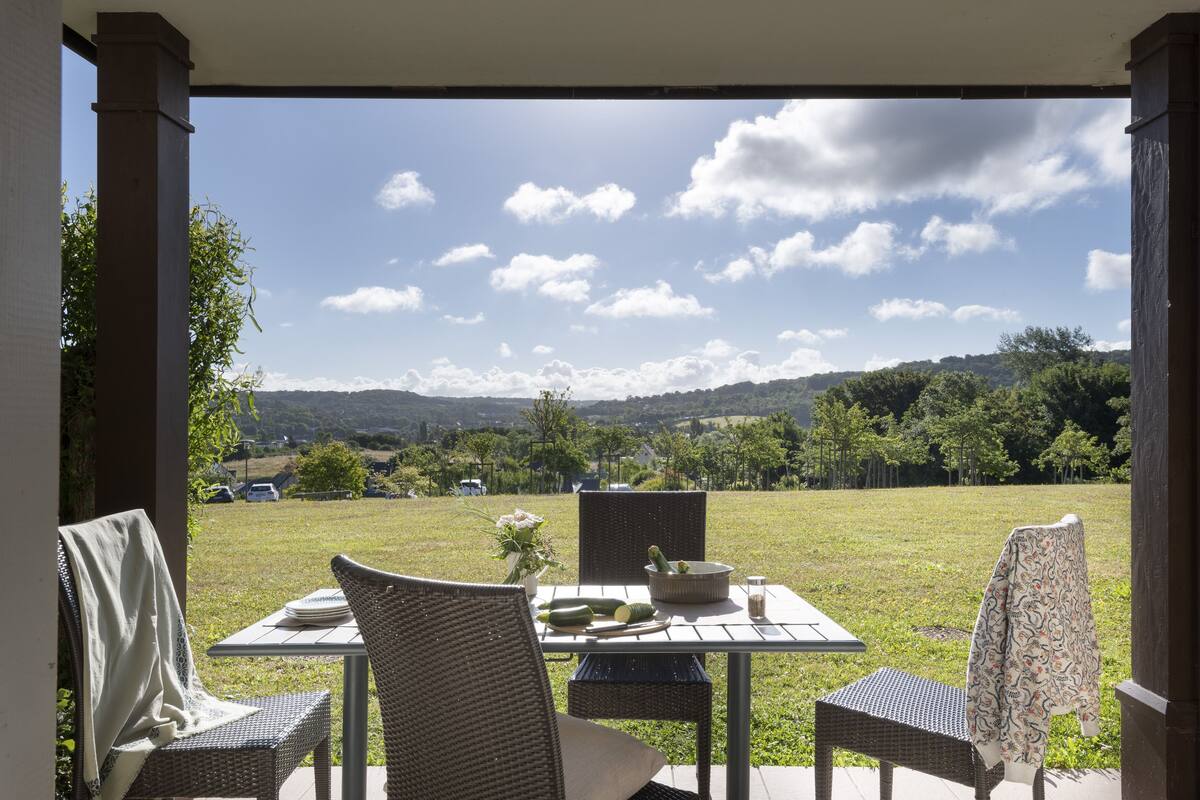 Eine überdachte Terrasse mit Korbmöbeln, einem Tisch, der mit Tellern, einer Schüssel und einem Glas gedeckt ist.