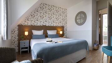 A bedroom with a large bed, two bedside tables with lamps, a wicker chair, a blue armchair, and a window with curtains.