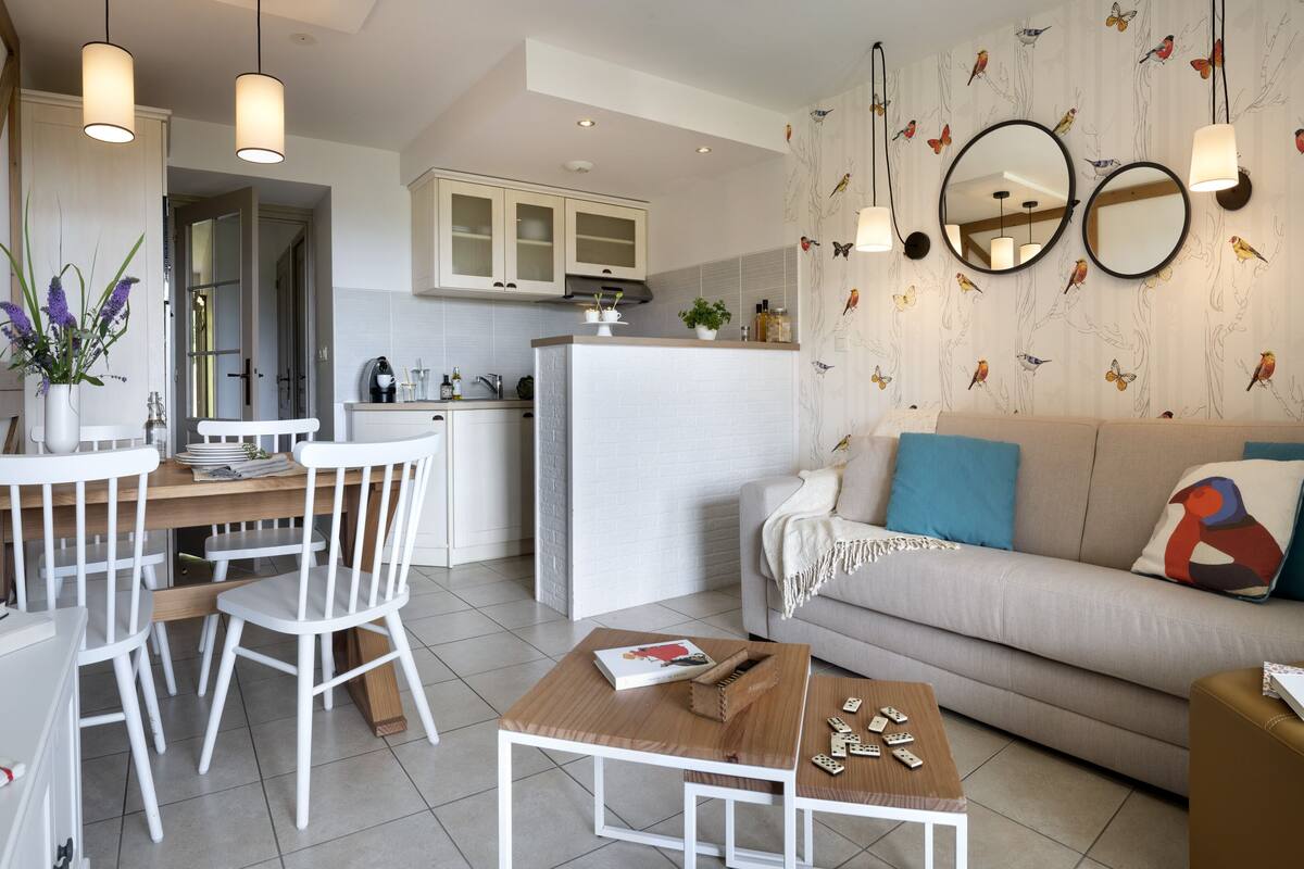 Eine moderne Küche mit weißen Schränken, ein Essbereich mit einem weißen Tisch und Stühlen sowie ein Wohnzimmer mit einer Couch und einem Couchtisch.