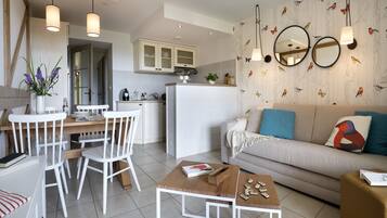 A modern kitchen with white cabinetry, a dining area with a white table and chairs, and a living room with a sofa and a coffee table.