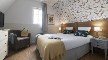 Un dormitorio con cama, mesitas de noche, televisor, una silla y una ventana.