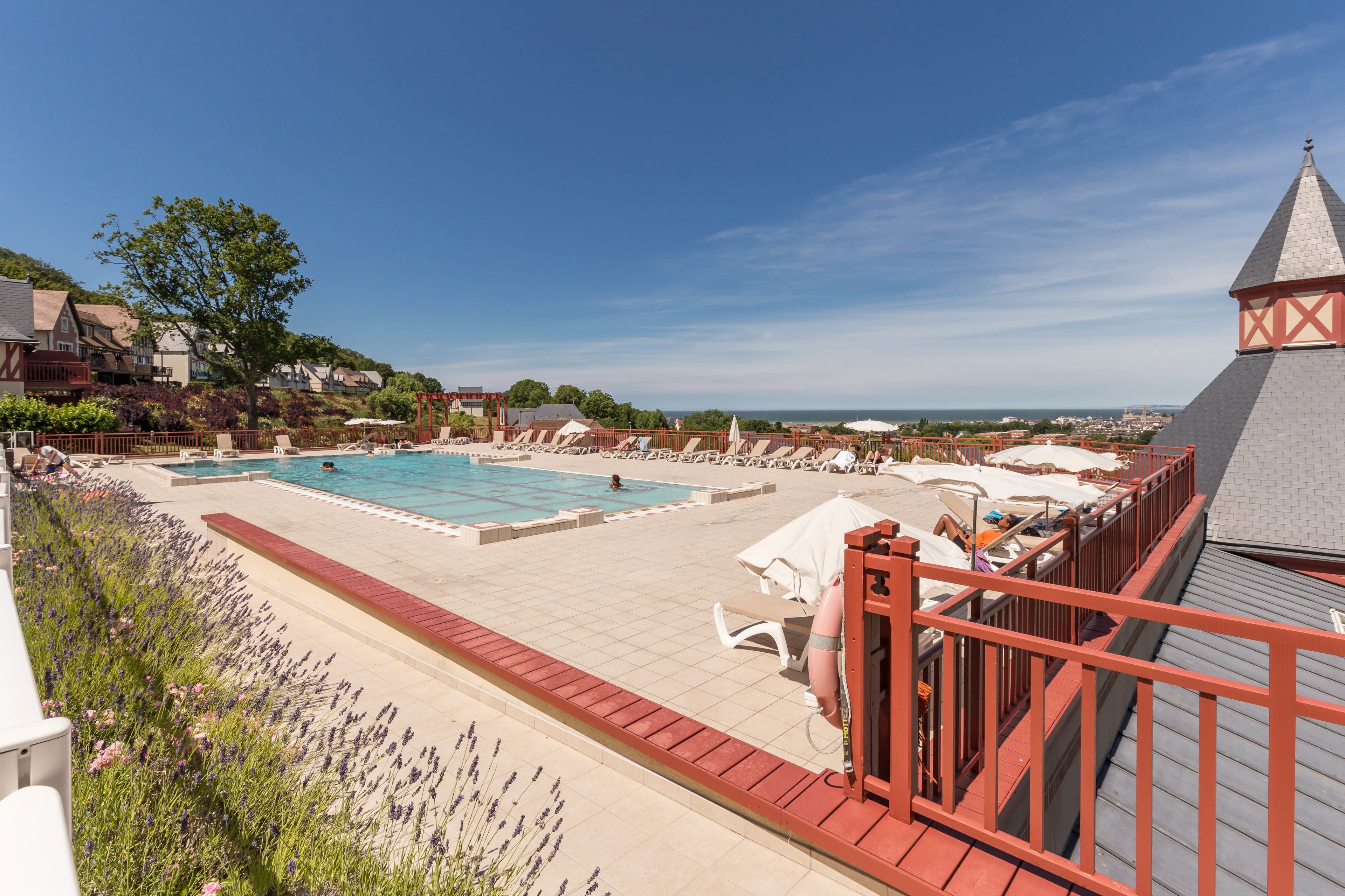 Un área de piscina en la azotea con varias piscinas, sillas de descanso y una barandilla roja.