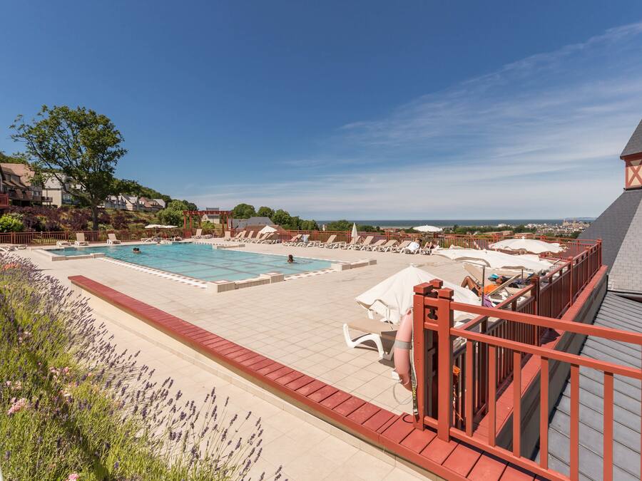 Ein Poolbereich auf dem Dach mit mehreren Schwimmbecken, Liegestühlen und einer roten Brüstung.