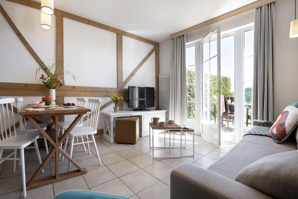 Ein modernes Wohnzimmer mit einer Couch, einem Esstisch mit Stühlen, einem Fernseher und einem Balkon mit Blick.
