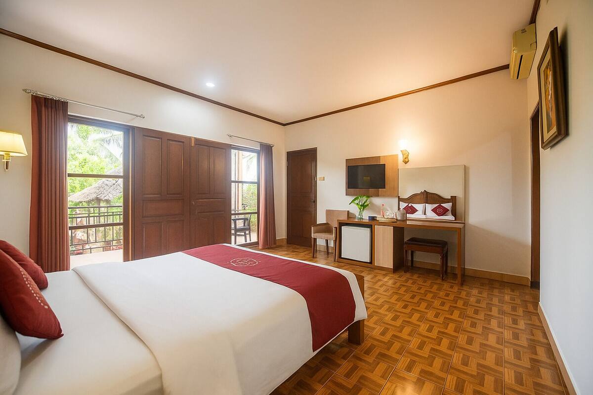A hotel room with a bed, desk, chair, TV, and a balcony.
