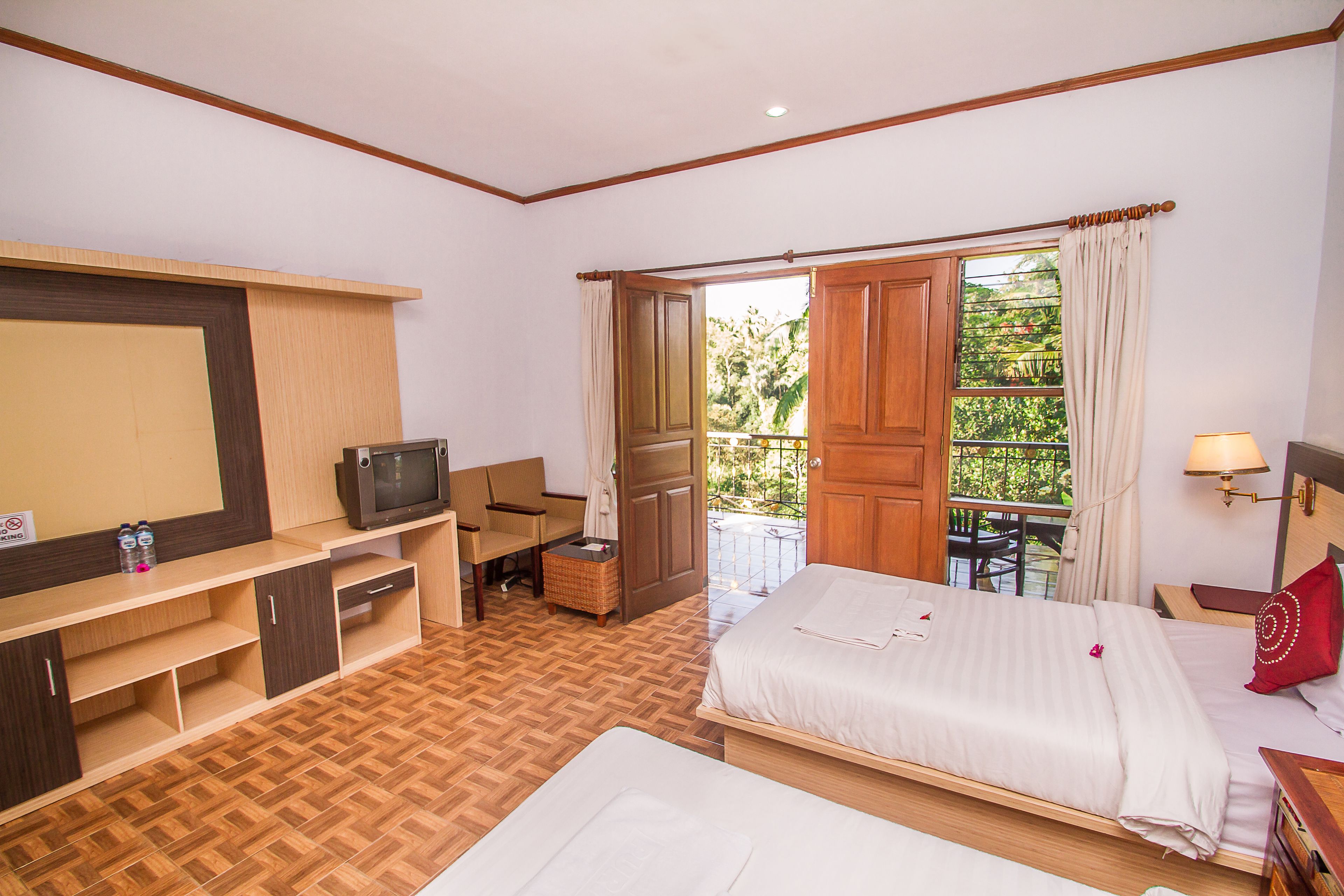 Une chambre d’hôtel comprenant un lit, un bureau avec une télévision, une chaise, une petite table et une fenêtre donnant sur un paysage verdoyant.
