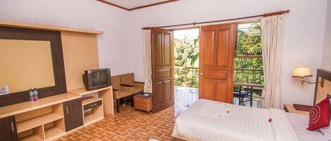 Une chambre d’hôtel comprenant un lit, un bureau avec une télévision, une chaise, une petite table et une fenêtre donnant sur un paysage verdoyant.