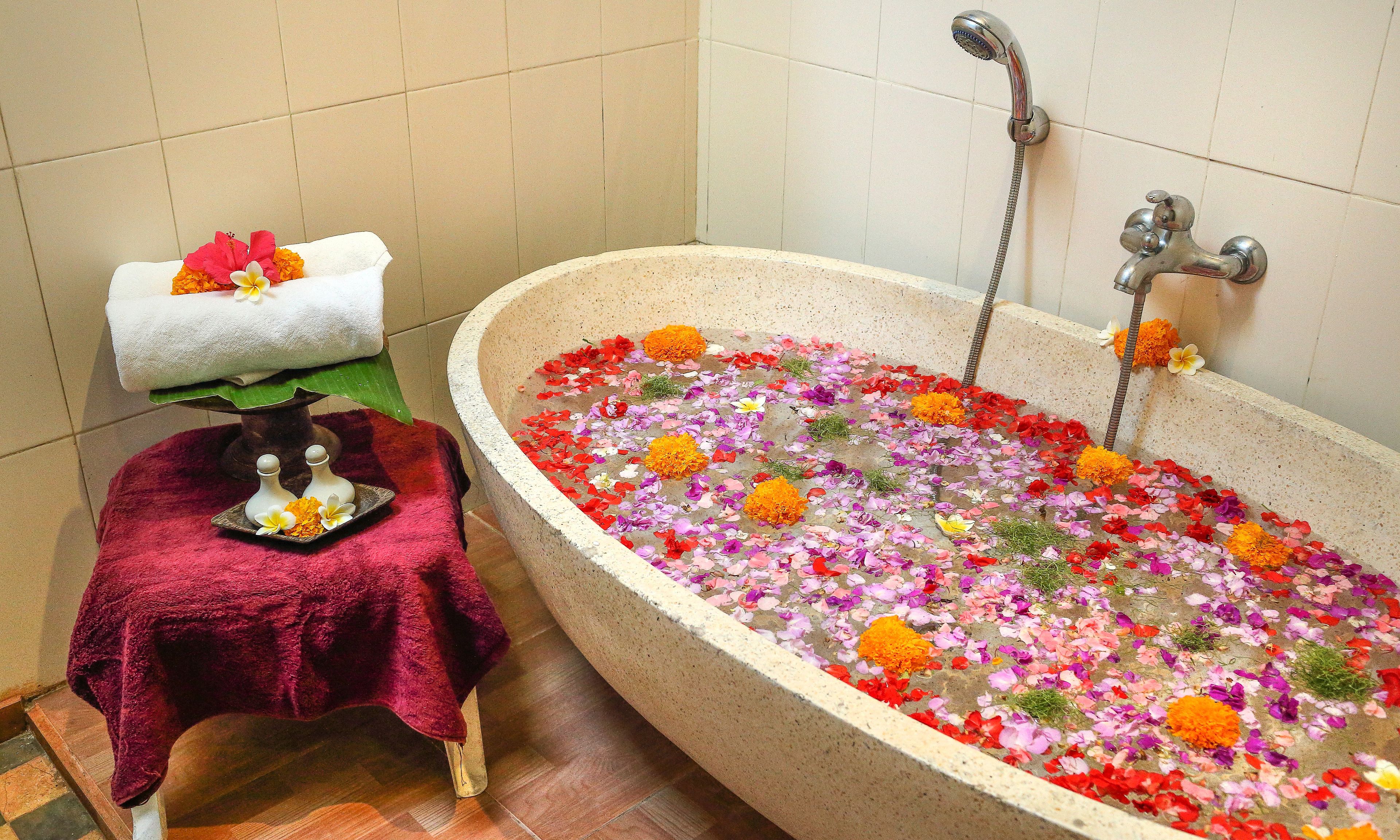 A bathtub filled with water and flower petals, a towel with flowers, and a small table with a red cloth.