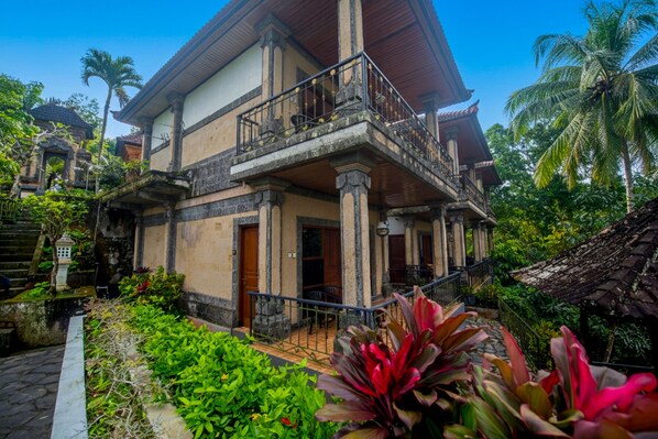 A two-story building with a balcony, surrounded by lush greenery and palm trees. - Puri Saron Hotel Madangan (Gianyar)