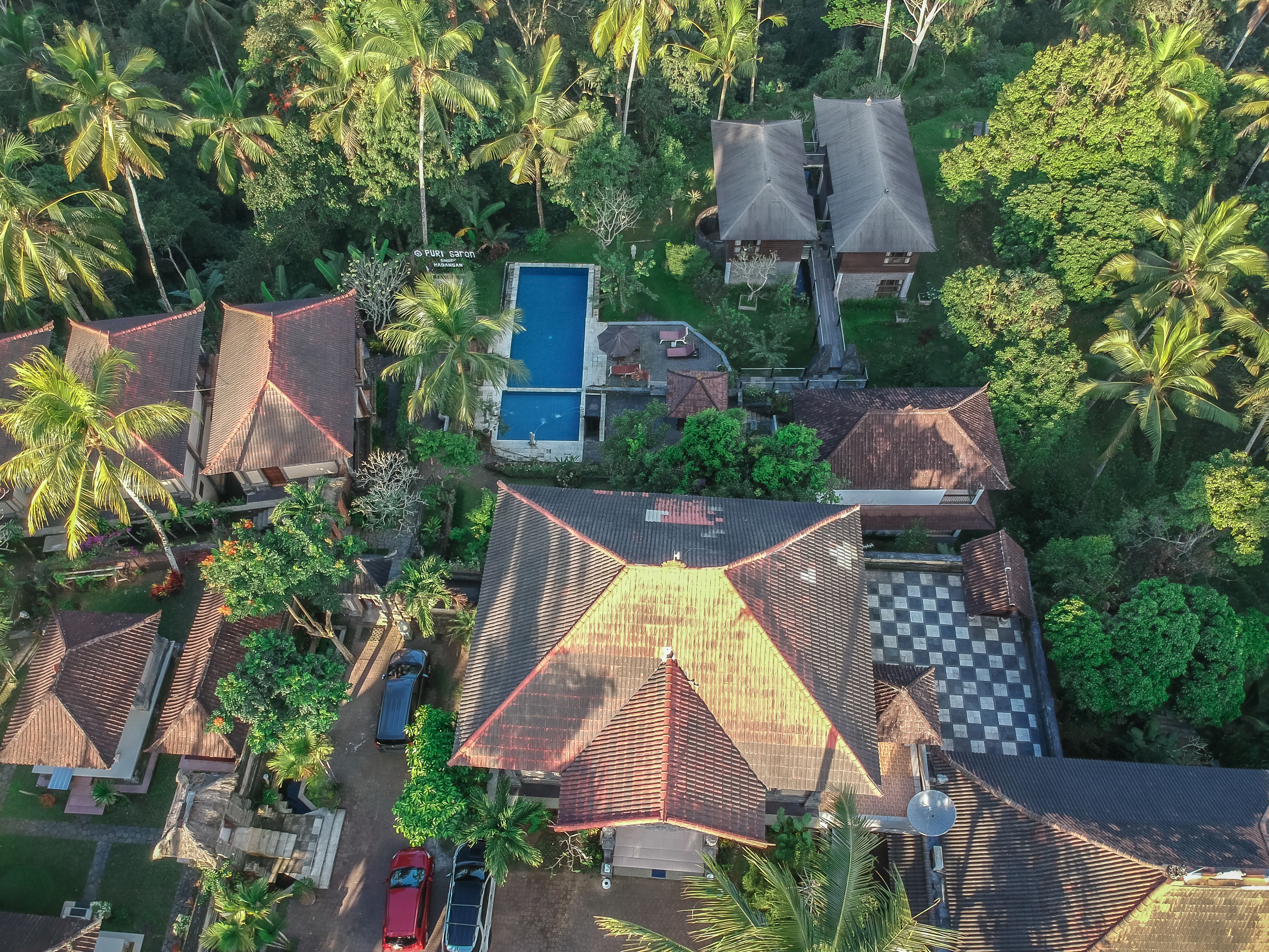 An aerial view of a resort with multiple bungalow-style buildings, a swimming pool, and lush tropical vegetation.