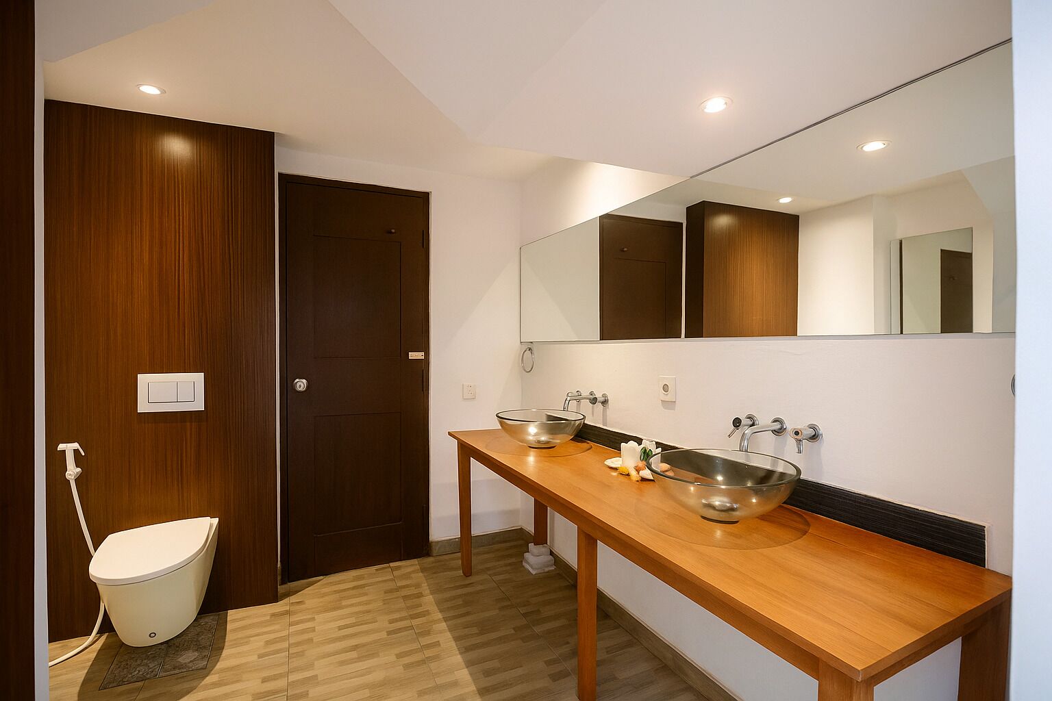 A modern bathroom with a wooden vanity, two stainless steel sinks, a toilet, and a large mirror.
