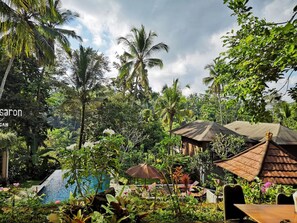 Een tropisch resort met een zwembad, weelderige begroeiing en een traditionele constructie met rieten dak.