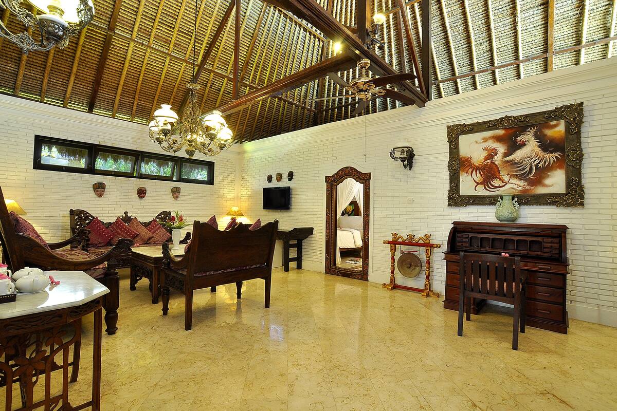 A spacious room with a high ceiling, wooden beams, a chandelier, a large mirror, and a traditional wooden desk.