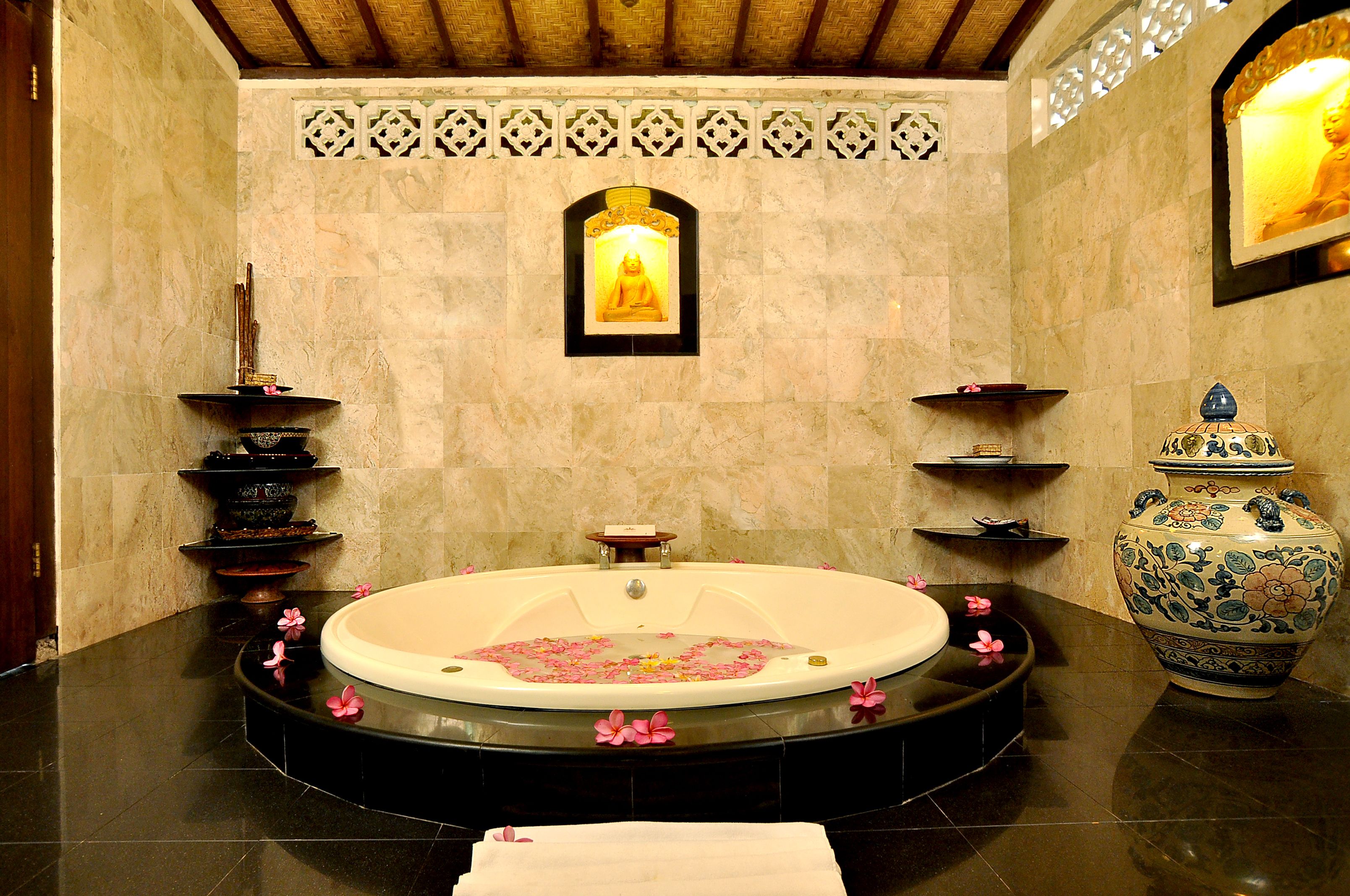 A spa room with a large bathtub, decorative shelves, a Buddha statue, and a large vase.
