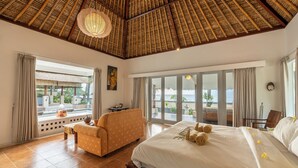 Un dormitorio amplio con una cama grande, un sofá y vistas al océano a través de amplios ventanales.