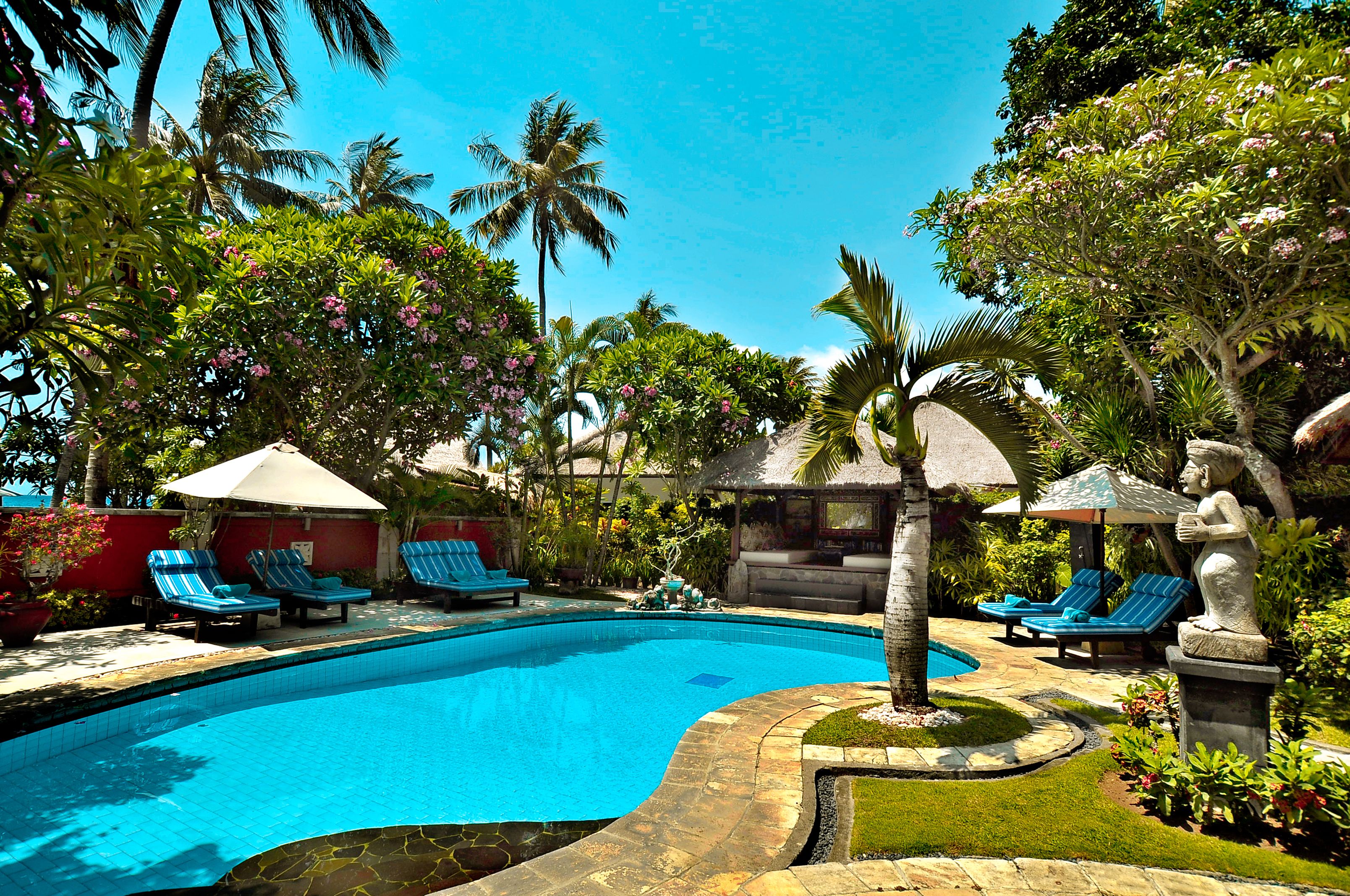 A swimming pool with lounge chairs and a statue, surrounded by tropical vegetation and palm trees.