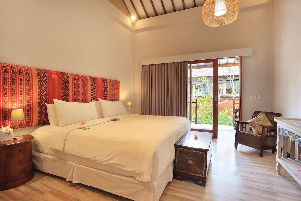 A spacious bedroom with a large bed, a wooden nightstand, a dresser, and a view of the outdoors through a sliding door.