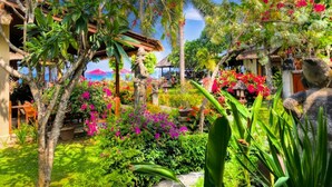 Un jardín tropical con vegetación exuberante, plantas en flor y una estructura con techo de paja.