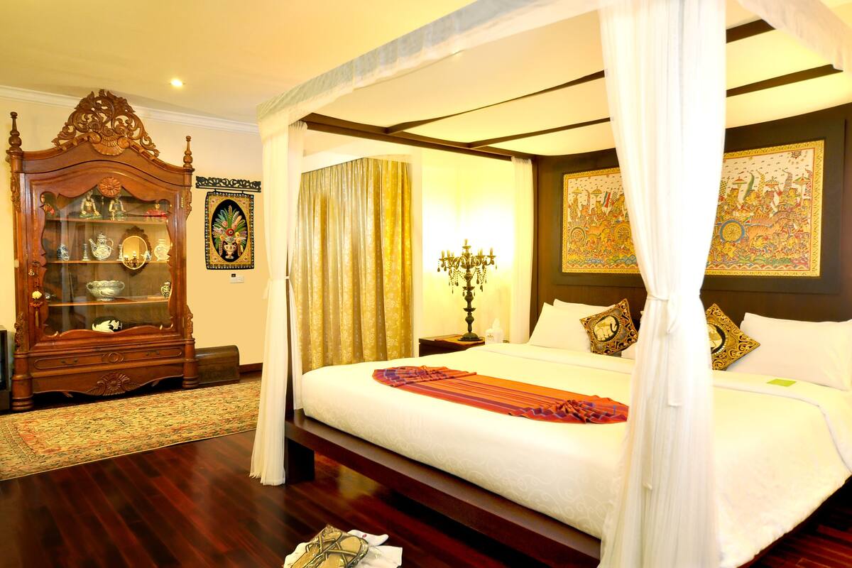 A traditional four-poster bed with a canopy, a wooden cabinet with glass doors, and a patterned rug.