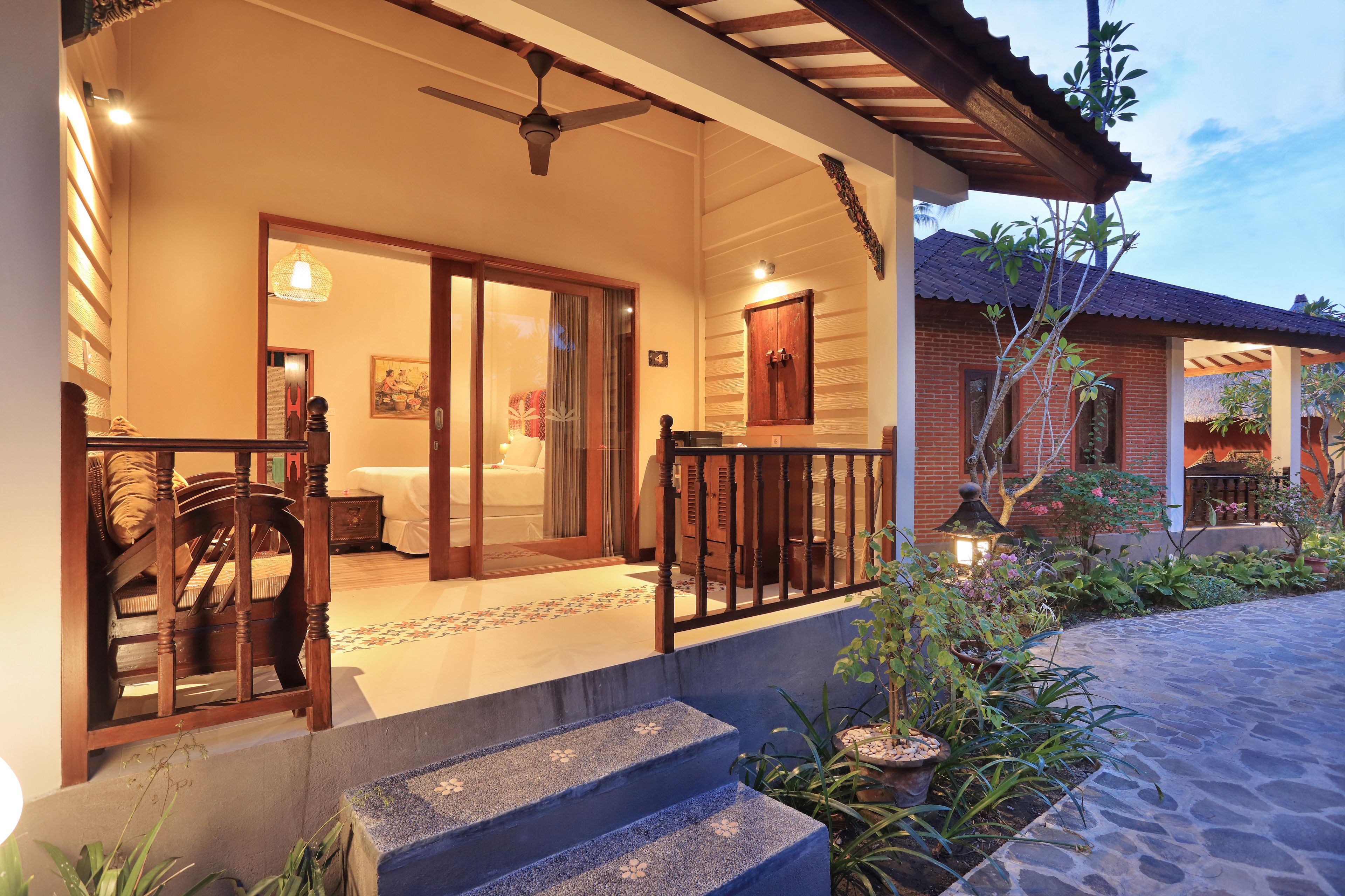 A well-lit entrance with a wooden porch, a ceiling fan, and a staircase leading to the main building.