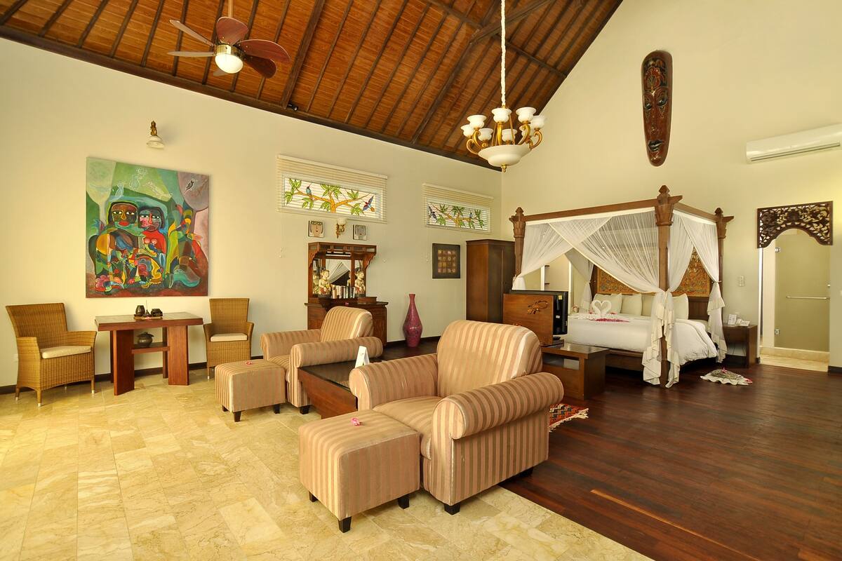 A spacious room with a large bed, a sitting area with chairs, a wooden floor, and a ceiling fan.