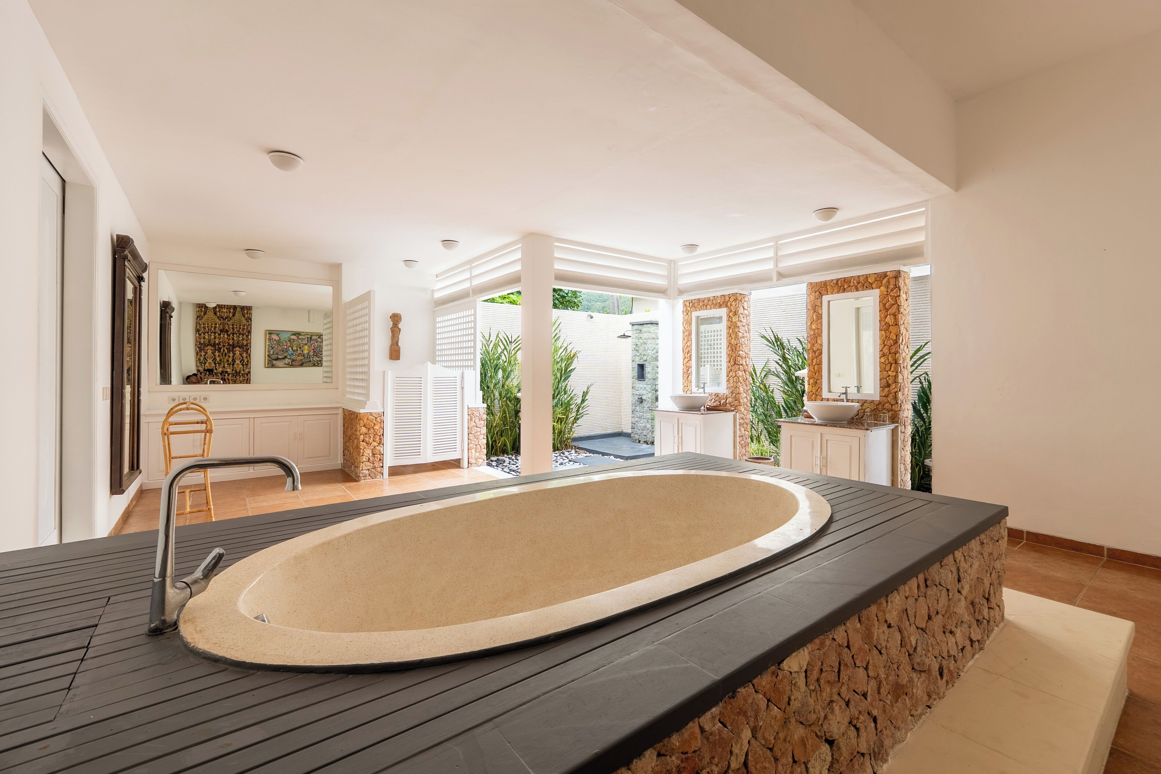 Een moderne badkamer met een groot bad, een accentmuur van steen en uitzicht op een tuin.