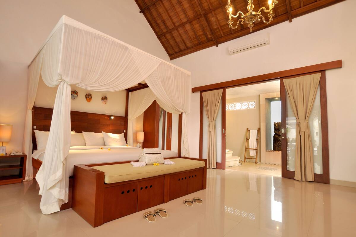 A spacious bedroom with a four-poster bed, a wooden bench, and a large mirror.