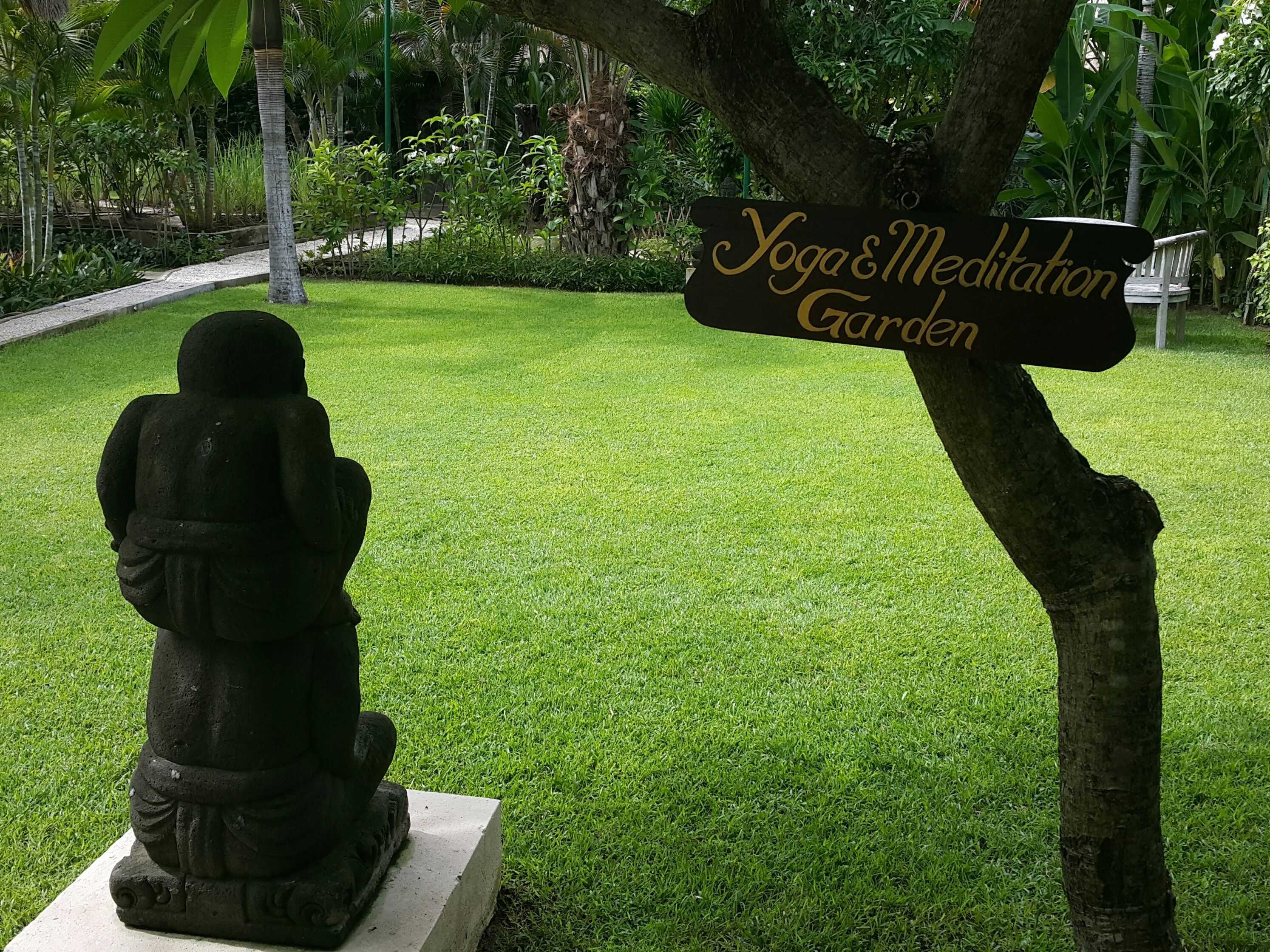 Uma estátua de uma figura sentada em um jardim, com uma placa que diz 'Jardim de Yoga e Meditação'.