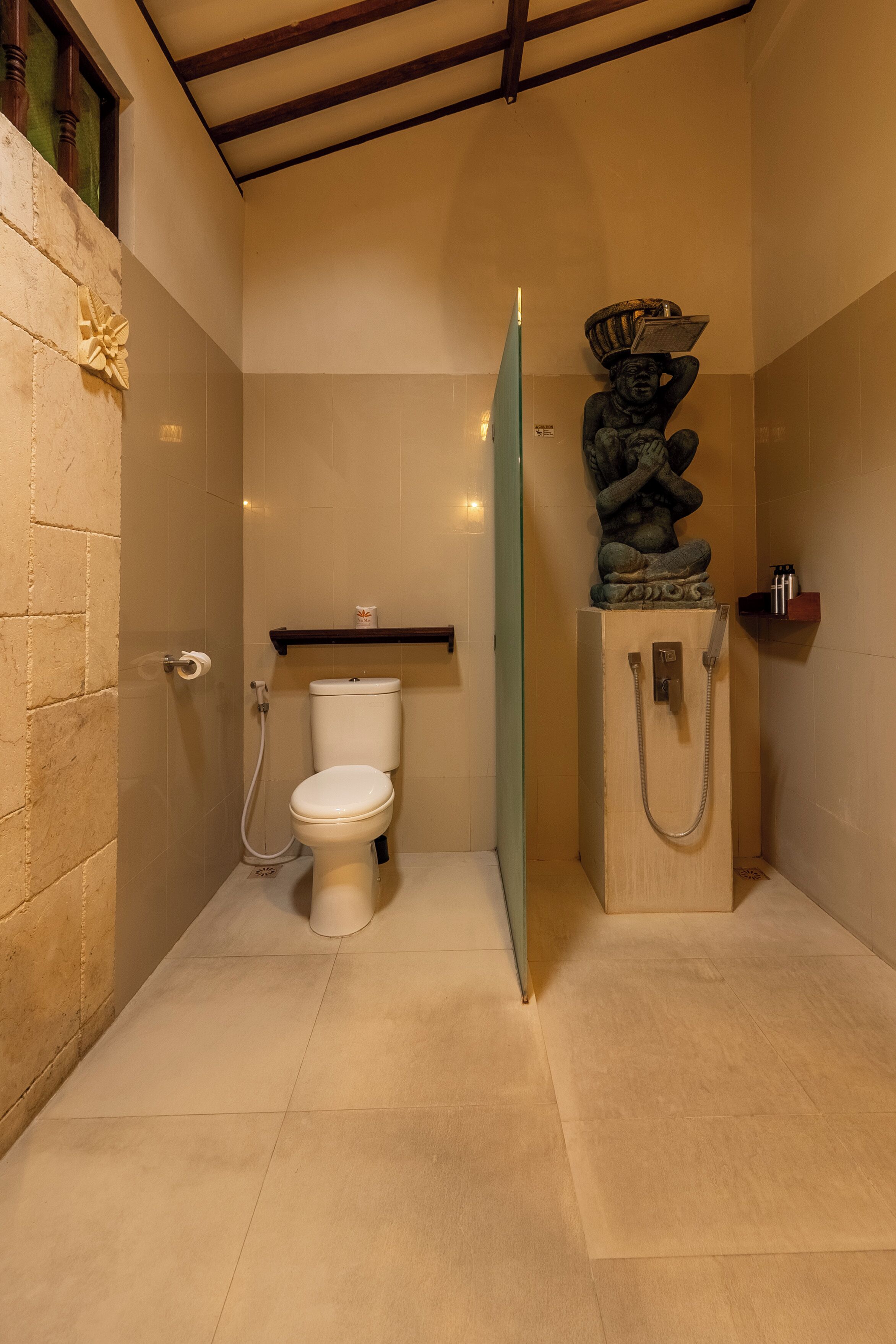 A bathroom with a toilet, a shower, and a decorative statue.