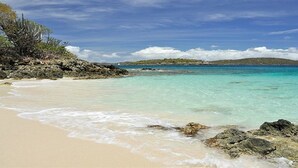 A beach with clear turquoise water, sandy shore, and rocky outcrops.